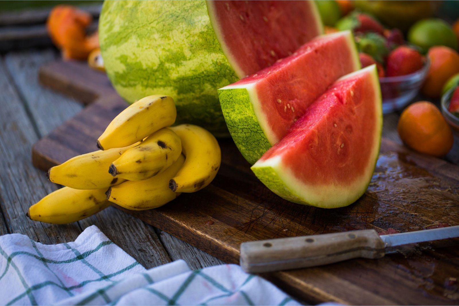 As bananas ricas em potássio encontram-se ao lado de uma melancia cortada em tábua de cortar, rica em L-citrina